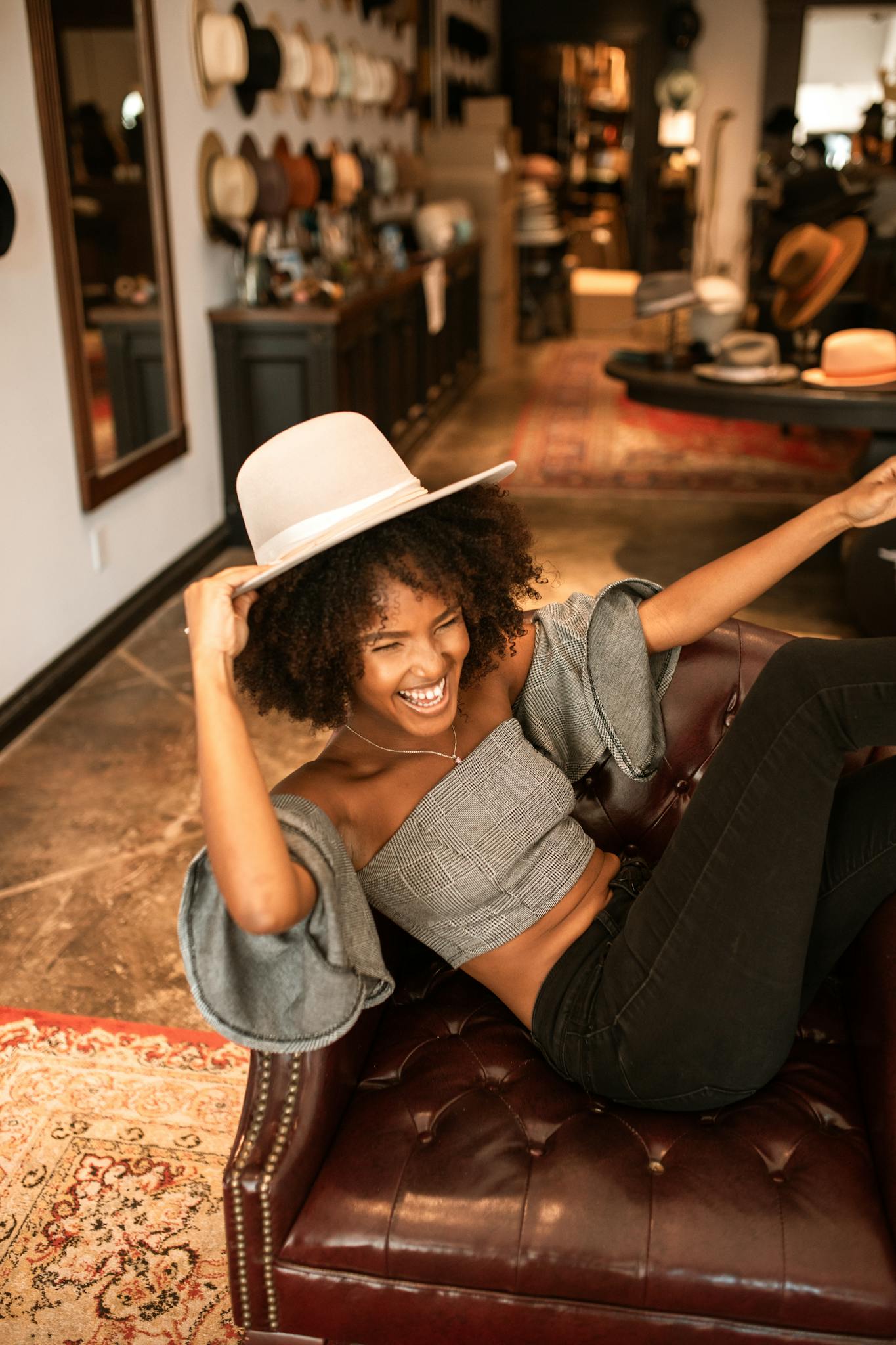 African American woman sitting happily in a&nbsp;stylish boutique, trying on hats and having fun.