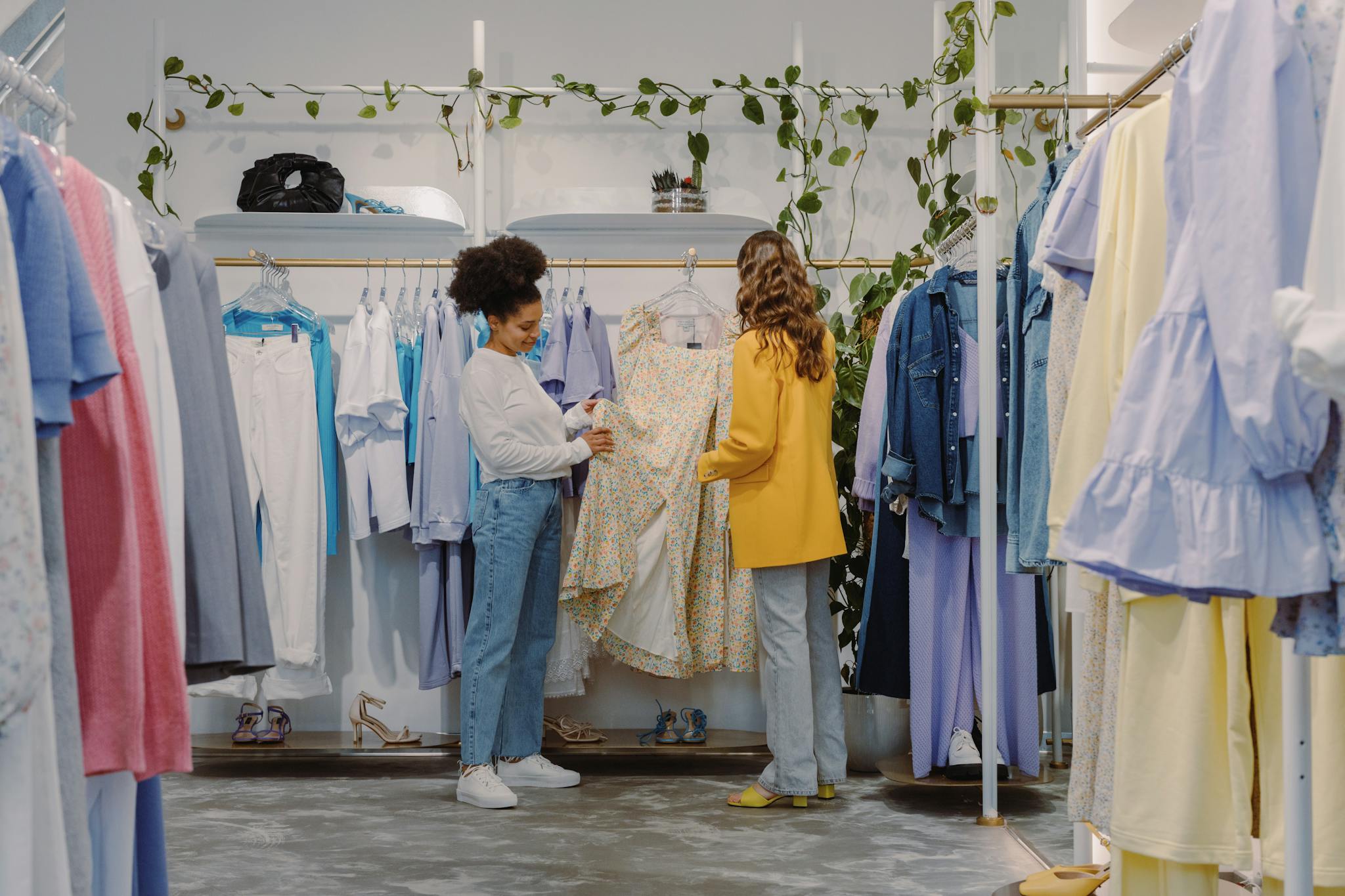 Two women shopping for trendy outfits in a&nbsp;modern clothing boutique filled with colorful garments.